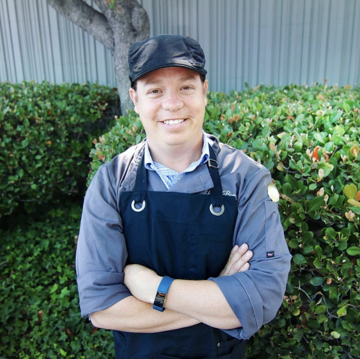 Oscar Gonzalez Headshot , wearing blue shirt, apron, black watch and black hat